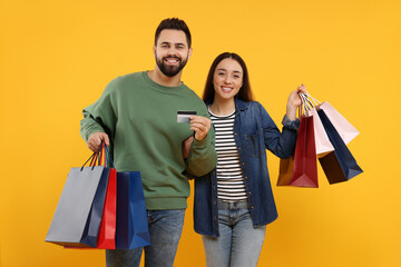 Happy couple with shopping bags and credit card on orange background