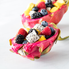 Dragon fruit shells filled with fresh fruit salad, against a white background.