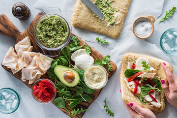 A board of fresh ingredients with hands preparing a turkey pesto wrap beside.