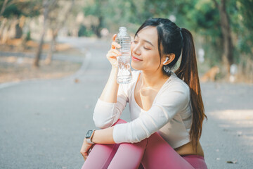 Fototapeta premium A young woman enjoys a peaceful moment, holding a clear water bottle with a gentle smile, as she takes a hydration break during an outdoor workout, wearing a smartwatch, wireless earbuds.