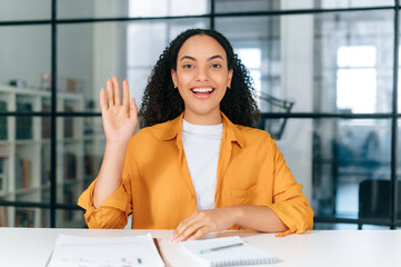 Positive hispanic or brazilian curly haired young woman, communicates via video conference, listens...