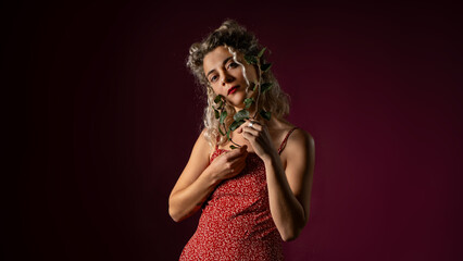Obraz na płótnie Canvas WOMAN WITH CURLERS IN RED OUTFIT HOLDING LAUREL LEAVES IN A PHOTO STUDIO