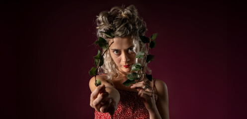 WOMAN WITH CURLERS IN RED OUTFIT HOLDING LAUREL LEAVES IN A PHOTO STUDIO