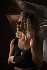 woman WITH WHITE CURLERS with an open umbrella over her head wearing a BLACK suit posing in PHOTO STUDIO