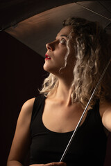 woman WITH WHITE CURLERS with an open umbrella over her head wearing a BLACK suit posing in PHOTO STUDIO