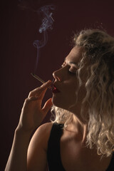 Fototapeta premium WOMAN WITH CURLERS IN A DARK ENVIRONMENT SMOKING A CIGARETTE WITH BACKLIGHT