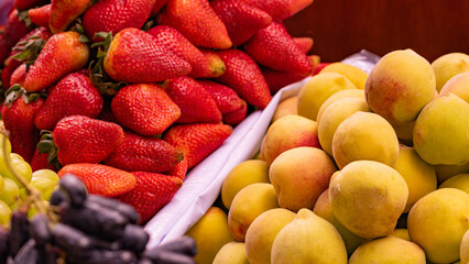 Fresh strawberries and peaches on display at a market stall, featuring vibrant colors and natural textures. Perfect for food and healthy eating projects.