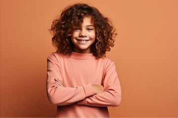 Cute little girl with curly hair smiling at camera over brown background