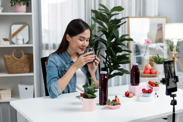 Smiling young beautiful Asian reviewing tasty mixed strawberry and cherry juice detox drinks,...