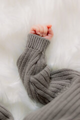 A baby's hand with his fingers curled up. The baby wears a gray sweater against a white background.
