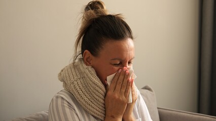 Sick woman wrapped in scarf coughing sneezing battling virus Shows symptoms of virus seeking relief Home care for virus evident in her discomfort Virus symptoms highlight need for rest and recovery