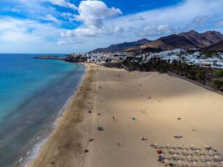 Fototapeta na wymiar White sandy beach and blue ocean water in Morro Jable vacation village on south of Fuerteventura, Canary islands, Spain