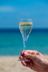 Hand with glass of cava or champagne sparkling wine on vacation, Dunes Corralejo sandy beach, Fuerteventura, Canary islands, blue ocean