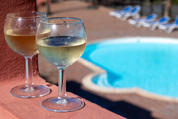 Glasses of cold white wine on roof terrace served outdoor in Corralejo, Fuerteventura in sunny day, pool with blue water