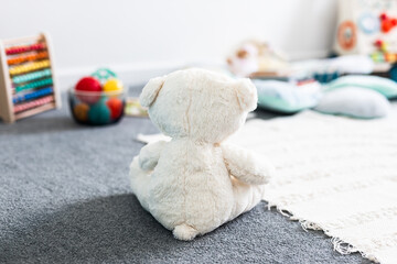 white teddy bear seen from behind in beautiful happy and messy nursery or children's room with...