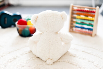 white teddy bear seen from behind in beautiful happy and messy nursery or children's room with colorful wooden toys and soft pillows and rugs, childhood learning or home decor