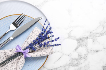 Cutlery, napkin, plates and preserved lavender flowers on white marble table, top view. Space for...