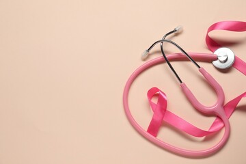 Fototapeta premium Breast cancer awareness. Pink ribbon and stethoscope on beige background, flat lay. Space for text
