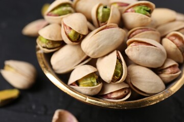 Tasty pistachios in bowl on black table, closeup