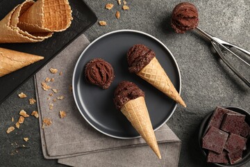 Chocolate ice cream scoops in wafer cones on gray textured table, flat lay