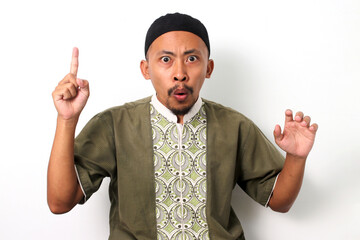 Excited Indonesian Muslim man in koko shirt and peci has an idea, raising his finger in a eureka...