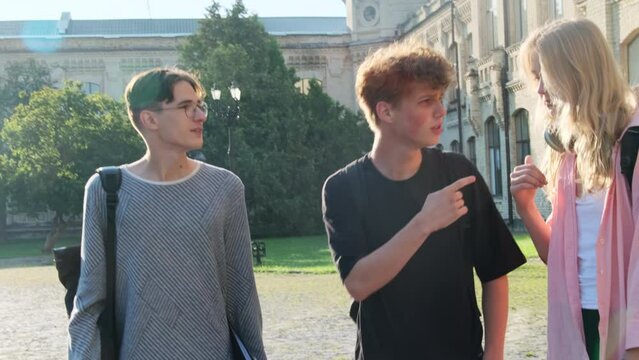 Curly haired young man tells story to friends leaving college. Students group walks against university campus after lessons finishing