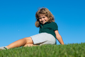 Portrait of a smiling child lying on green grass. Cute kid boy enjoying nature outdoors. Healthy carefree kid playing outside in summer park. Healthy kids outdoor lifestyle concept.