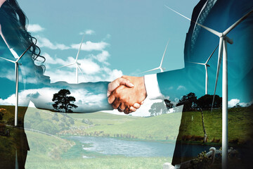 Double exposure graphic of business people handshake over wind turbine farm and green renewable...