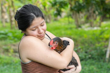 caucasian latina woman holding a chicken in her arms while looking at it with tenderness and love