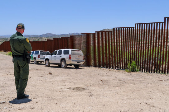 Two border patrol vehicles and a U.S. Customs and Border Protection agent stationed at the border fence with Mexico near Sasabe, Arizona