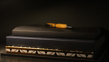 Moody and dark photo featuring a stack of books and journals with a fancy wooden pen on top - Still life photography