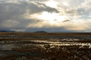 The rays of the setting sun break through the clouds of a storm front over the swampy steppe in early autumn.