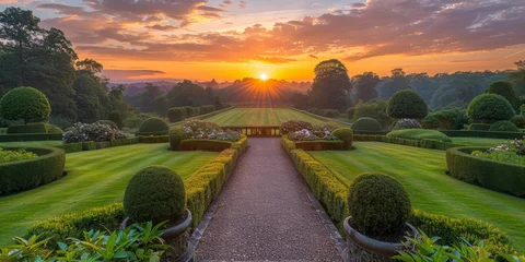  The sun is setting in the sky, casting a warm golden light over a manicured garden filled with colorful flowers and lush greenery. © Lidok_L