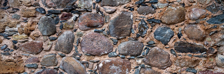 Ancient stone wall. Weathered rough masonry surface. The wall of the old castle. Wide panoramic texture for background and design.