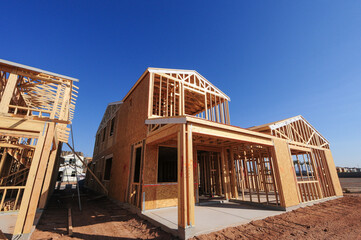 Wide-angle view of wooden single-family homes in different stages of construction in a new subdivision in southeastern Maricopa County, Arizona.