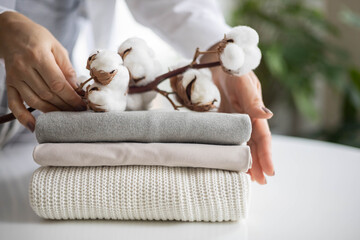 Women's hands hold a stack of neat, clean, cotton clothes in neutral shades. Branch with cotton...