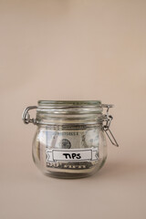 Saving Money In Glass Jar filled with Dollars banknotes. TIPS transcription in front of jar....