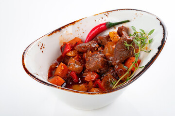Stew with beef and vegetables in a bowl on a white background. The dish is stewed over low heat with spices and gravy
