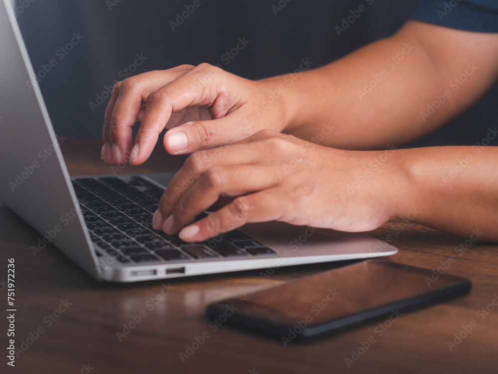 Poster close-up of hands typing on a laptop computer with a mobile phone on a wooden table.