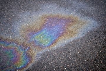 Close-up of an iridescent oil or gasoline spill on a wet asphalt, viewed from above. Bold...