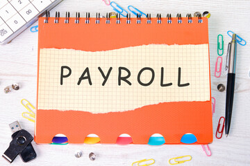 PAYROLL word on a piece of paper on an orange notebook