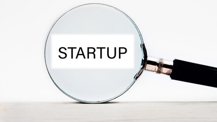 Startup - word concept through a magnifying glass on a white stripe on a light background