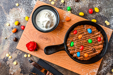 M and M Cookie Dough with mini chocolate candies, chocolate, whipped cream, knife and fork served...