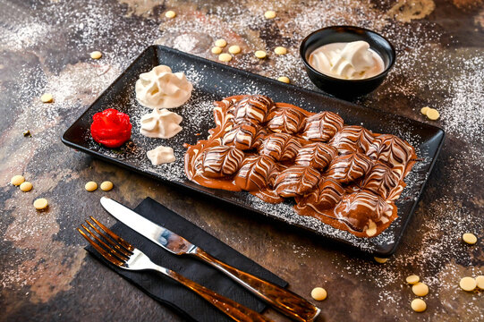 Marble Poffers with chocolate, whipped cream, knife and fork served in dish isolated on dark background closeup top view of cafe baked dessert food