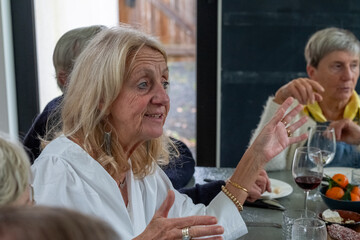 This image features a senior lady in a white blouse, her face animated with the thrill of sharing a captivating story. Her hands are expressively gesturing, highlighting the narrative's energy. A peer