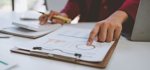 Asian businesswoman smiles at the idea of ​​working with a calculator to calculate income on laptop. Document. Statistics data from chart. A graph showing the financial growth of a company.