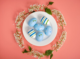 Easter composition. Easter eggs on a white plate, cherry branches in the shape of a circle. Pink background, copy space. View from above.