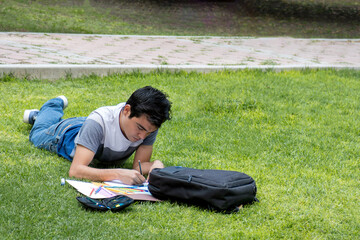 A male student lying on the grass writing on a piece of paper