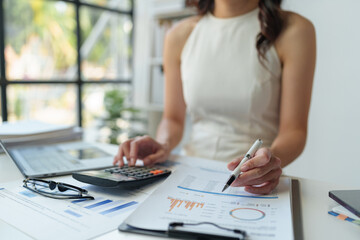 Asian female finance staff is pressing a calculator to calculate company sales and profit to report...