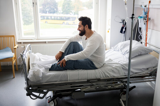 Smiling male patient sitting on bed in ward